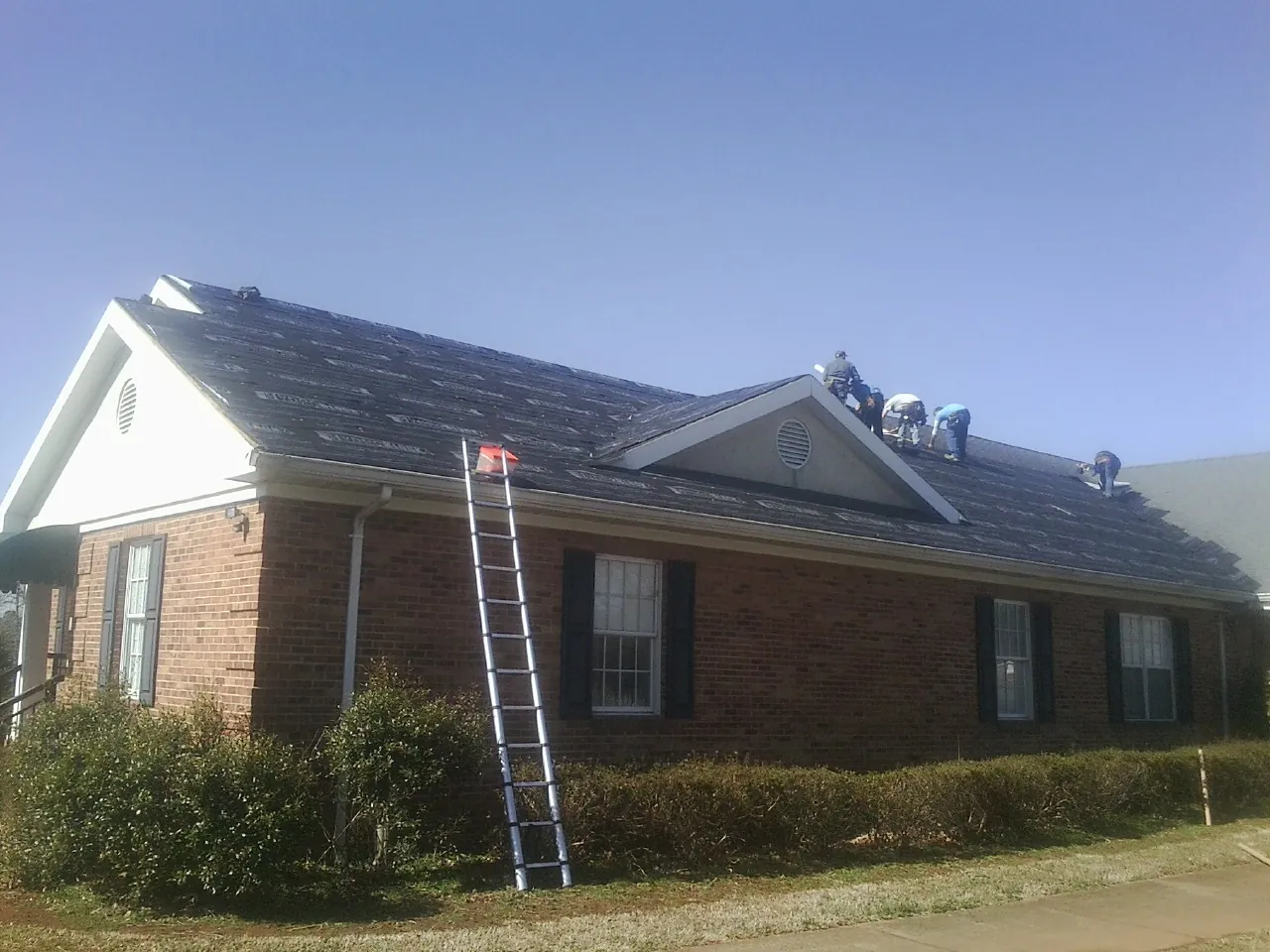 Crew tearing shingles off a brick ranch roof with a ladder set — Emergency Roof Repair work by our crew in Coplay