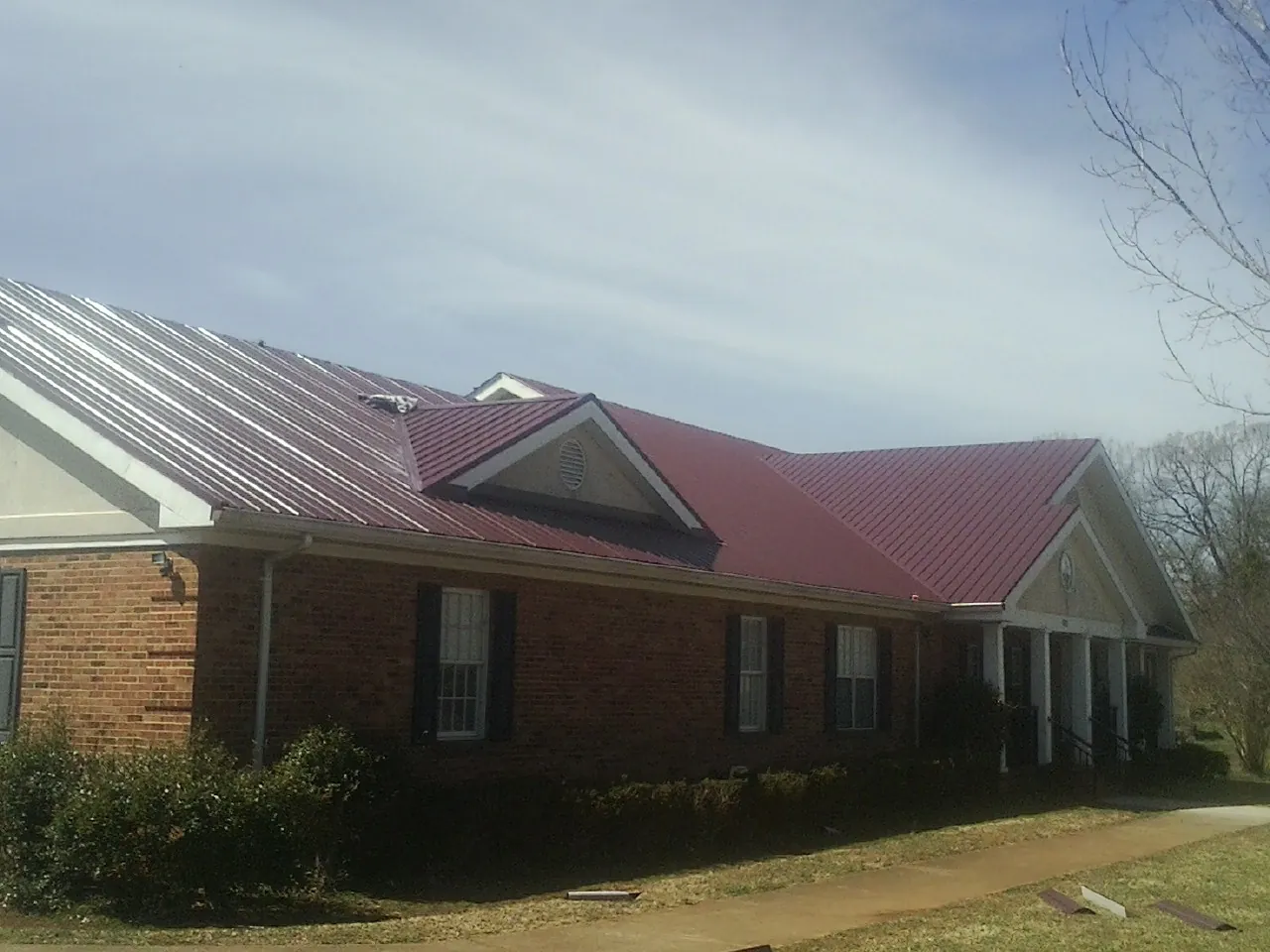 Red metal roof with gabled entries on a long brick building, from a Hail Damage Roof Repair job in Coplay