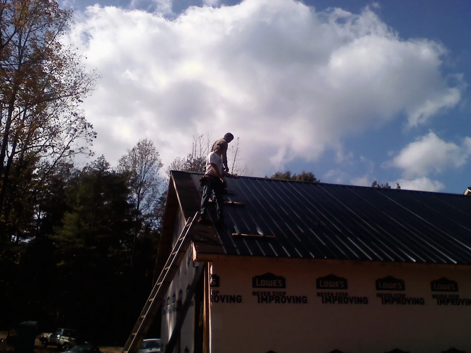 Roofer fastening dark metal panels high against a cloudy sky, from a Roof Inspection job in Coplay